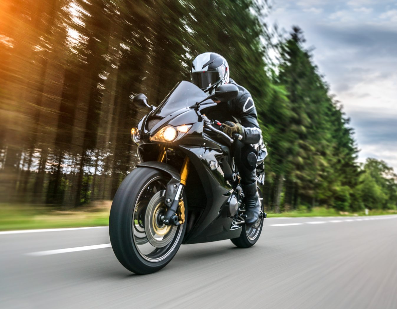 A black motorcycle with a full geared driver driving fast with motion blur forest trees.